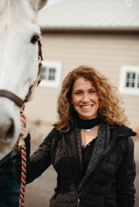 Anne Schwartz stands next to a white horse.