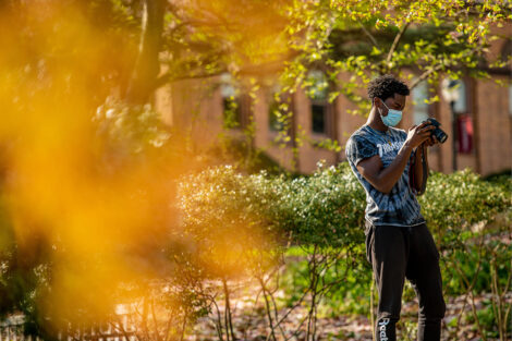 A masked student uses camera to take photos of campus.