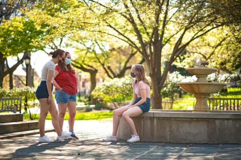 Three masked students converse in the courtyard behind Colton Chapel.
