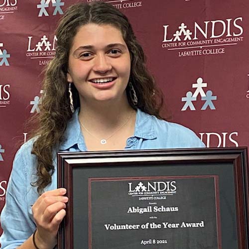 Abigail Schaus holds a framed certificate in front of the Landis Center logo