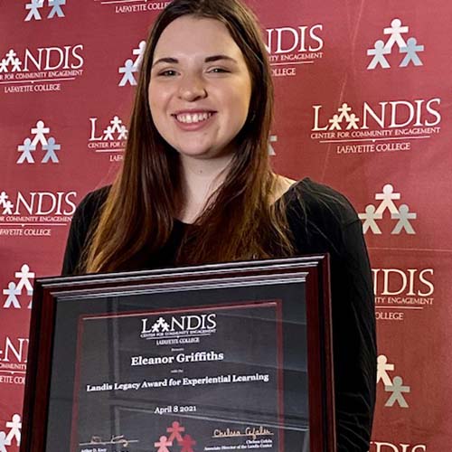 Eleanor Griffiths holds a framed certificate in front of the Landis Center logo