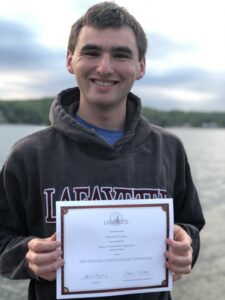 Michael O'Connor standing on a beach, holding his Eugene P. Chase Phi Beta Kappa Prize certificate from Lafayette College