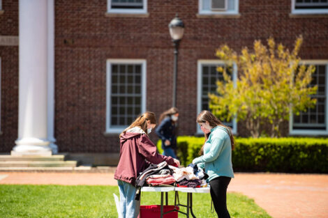 Students wearing masks look through clothing on a table in front of Watson Hall.