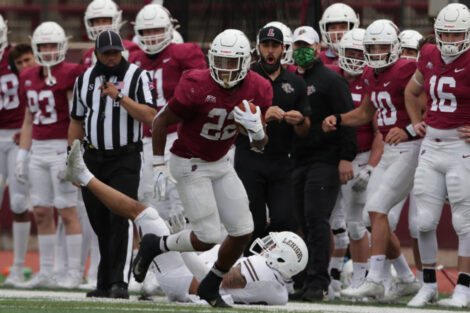 Lafayette College football player holds the football and runs on Fisher Field while crowd of players look on