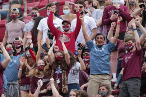 students in masks and leopard gear cheer on football players in Fisher Field stands