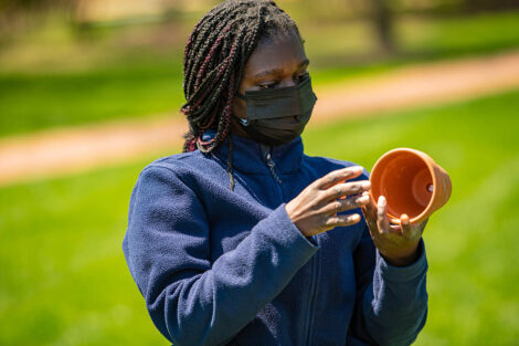 A student wearing a mask examines a pot to fill with soil.