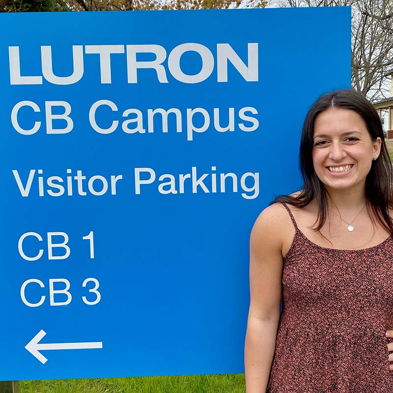Nicole Holzapfel leans against a blue sign that welcomes visitors to Lutron