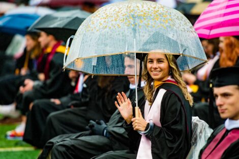 seniors in cap and gown on Fisher Field with umbrella