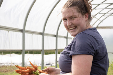 A student smiles, holding freshly picked carrots.
