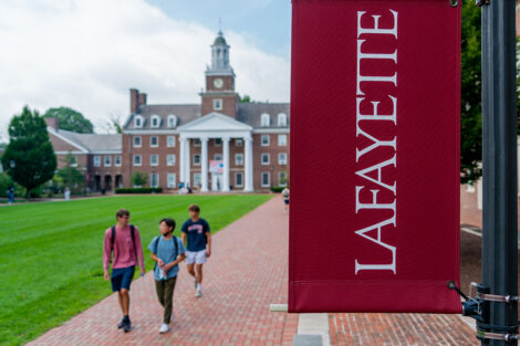Students walk in front of Watson Hall; a Lafayette College flag hangs on a pole beside the pathway.