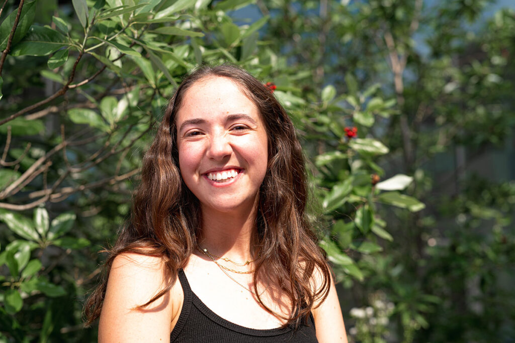 Kaela Marcus Kurn smiles in front of rich greenery.
