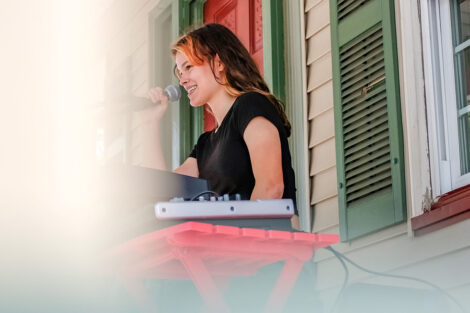 young person plays keyboard and sings on a porch
