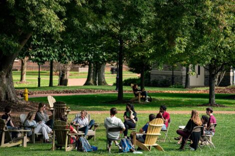 members of College community sit outside on the Quad in Adirondack chairs