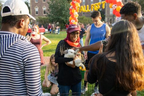 student in Lafayette cap smiles while holding a rabbit on the Quad, others look on and smile
