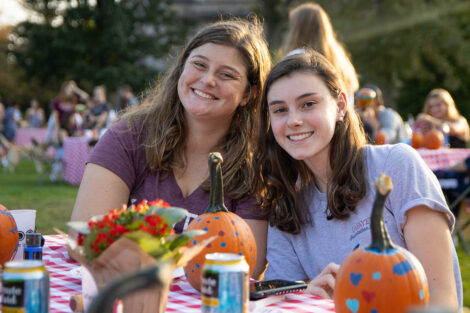 students smile at a table where they are painting pumkins