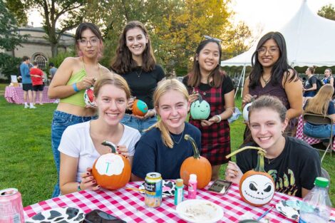 students smile at a table where they are painting pumkins