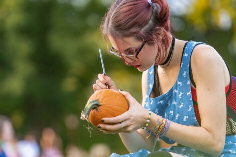 student sits on Quad grass and paints pumpkin