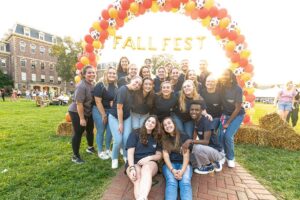 students gather in a group under Fall Fest balloon arch on Quad