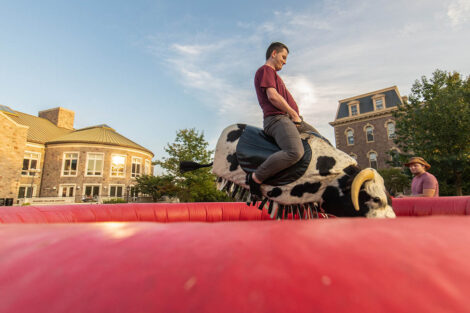student rides a mechanical bull on the Quad