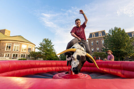 student on a mechanical bull smiles and raises hand in air