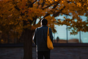 student faces away from camera and walks toward Skillman library, hint of orange foliage