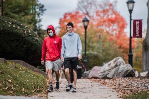 two students walk on an path on campus, hints of fall foliage behind them
