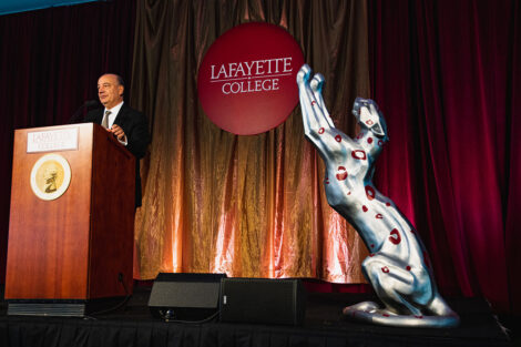 Robert E. Sell ’84 H’18, Chair of the Board of Trustees, speaks at a podium next to a Leopard statue.