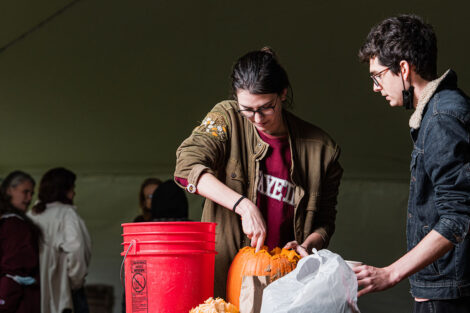 student carves pumpkin, another student looks on
