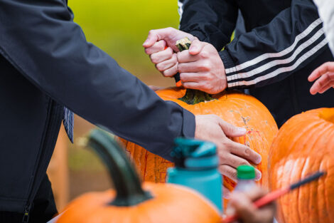 one student steadies a pumpkin while another carves into it