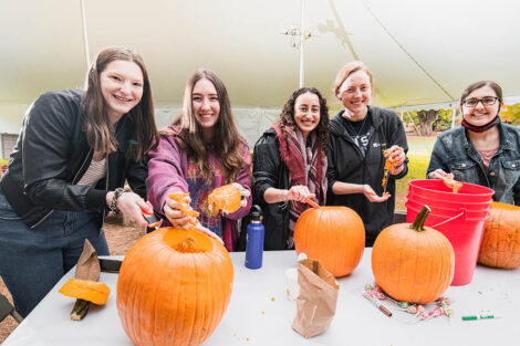 group of students stand at table with pumpkins and paint and smile