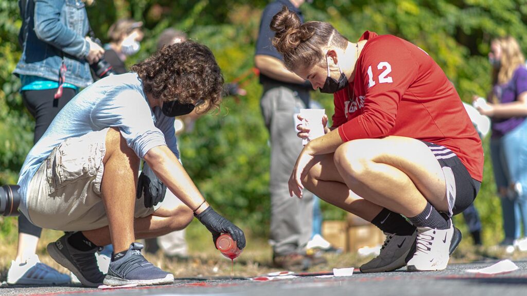 two Easton high students crouch down near pavement and pour red paint on the ground
