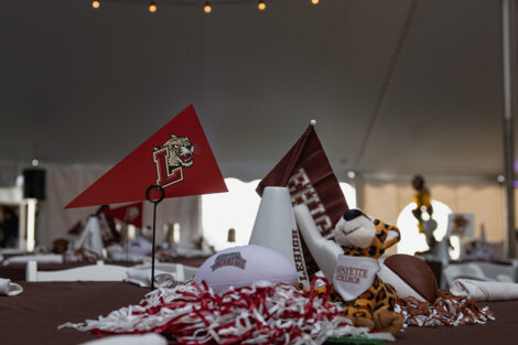 Lafayette and Lehigh small flags, footballs, and other memorabilia sit on a table under white tent with white string lights