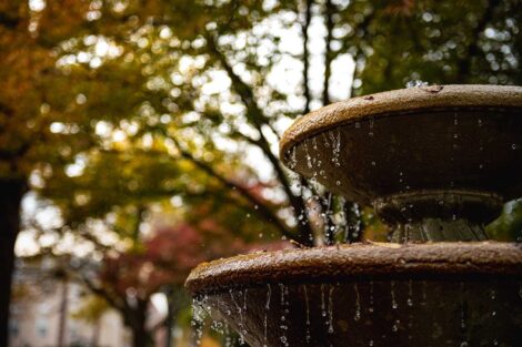 water drips down from a fountain, fall foliage in background