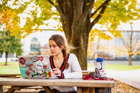student sits at picnic table with laptop and water bottle, golden foliage behind her