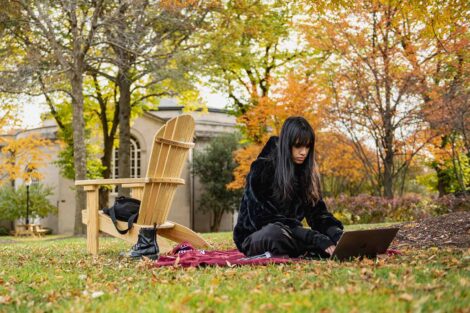 student sits on Lafayette blanket on Quad, works on laptop, fall foliage surrounds student