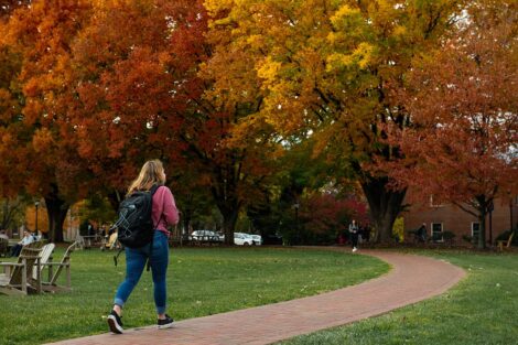 student carries backpack while walking on Quad pathway, orange, red, and yellow foliage