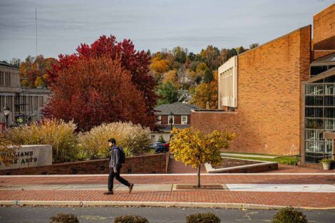 student walks past Williams Center for the Arts, foliage on College Hill is in background