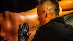 A tattoo artist creates a blood line on Rajas' back.