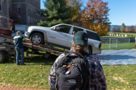 A person watches as an SUV gets loaded off of a tow truck and on to the Quad