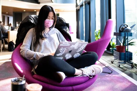 student sits in purple round chair and looks at laptop in Rockwell