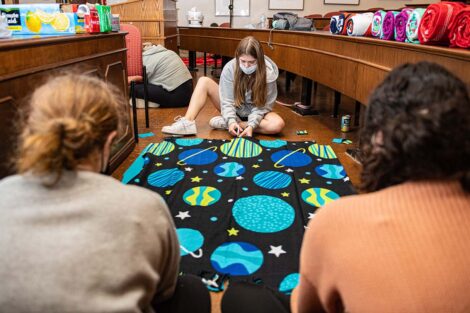 Three students work on a blanket. Two have their backs to the camera while one faces the camera