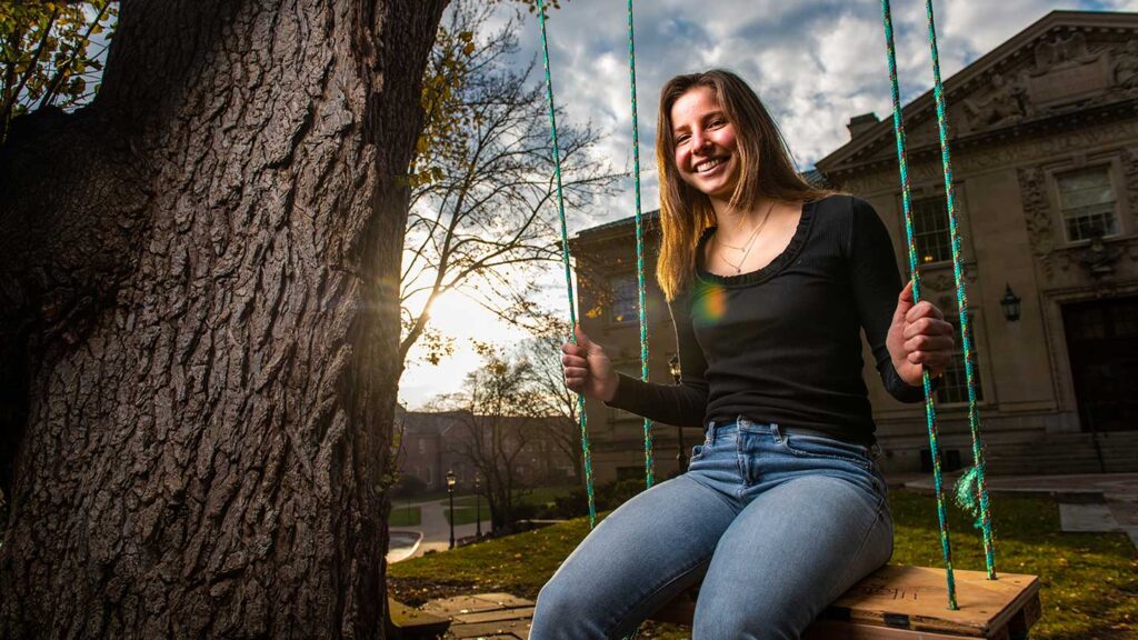 Student Kristen Steudel '22 sitting on a swing in front of Lafayette College's Kirby Hall of Civil Rights with sunset in the background