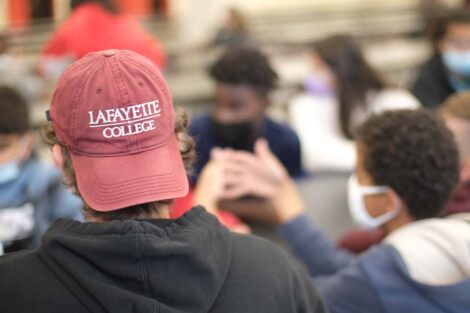 Sitting at a table with students is a Lafayette student wearing a Lafayette baseball cap turned backward