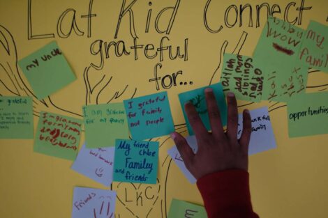 Hand places sticky note on yellow poster board filled with grateful notes