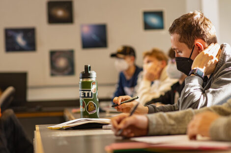 Students, wearing masks, take notes in a classroom.