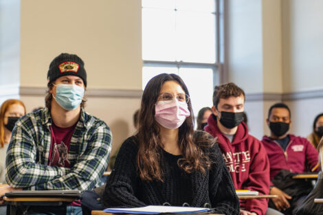 Students wearing masks, sit inside of a classroom.