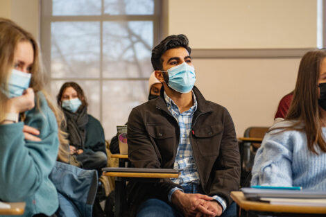 Students wearing masks, sit inside of a classroom.