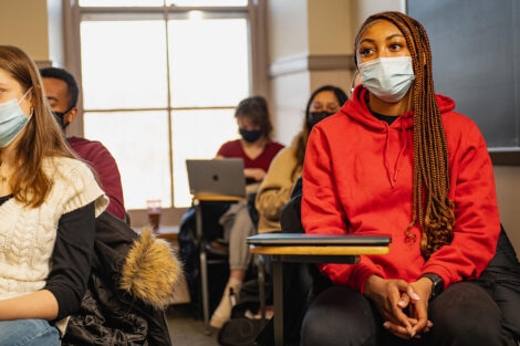 Students, wearing masks, sit inside of a classroom.