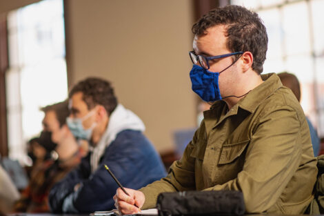 Students, wearing masks, sit inside of a classroom.