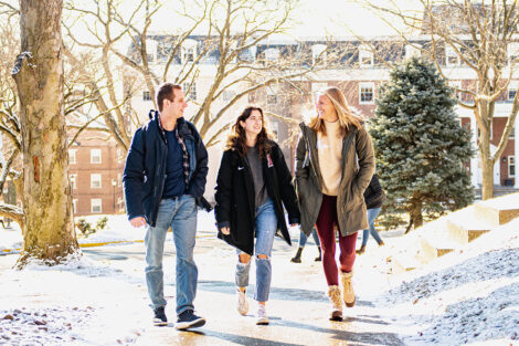 Three students walk along a path surrounded by snow.